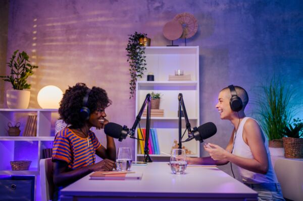 Two interracial podcasters are sitting in a home broadcasting studio